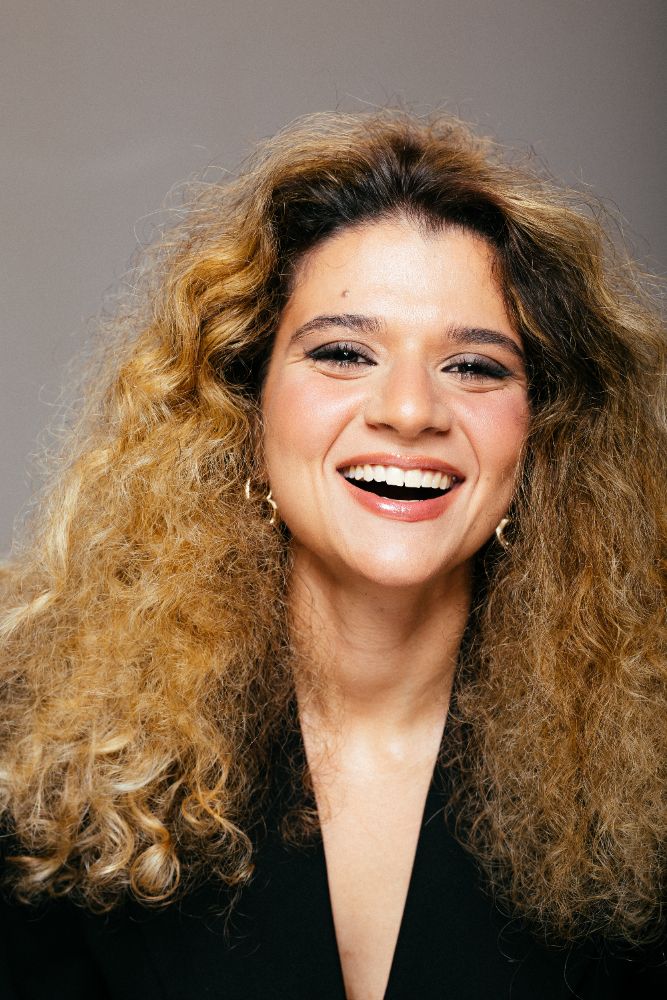 Atriz sorrindo, cabelos cacheados