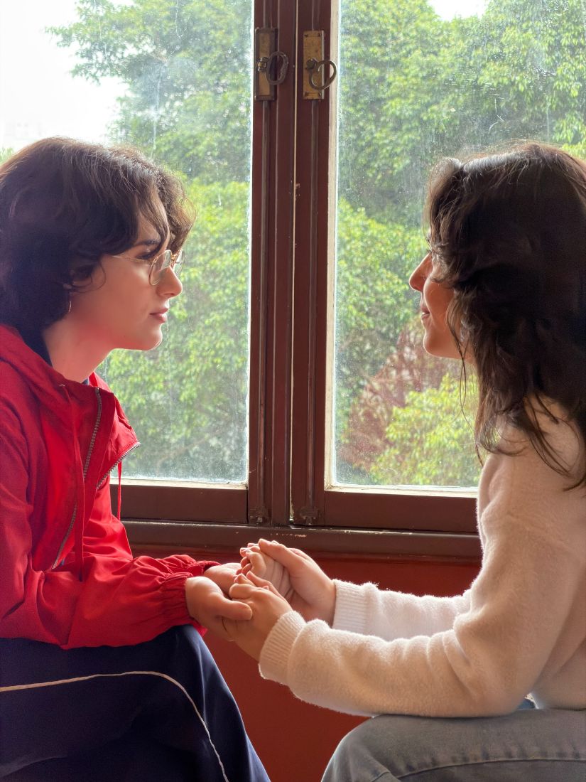 Duas atrizes de mãos dadas junto à janela